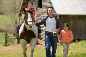 Father and sister assisting boy horseback riding